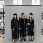 Group graduation portrait with caps and gowns in gymnasium setting.